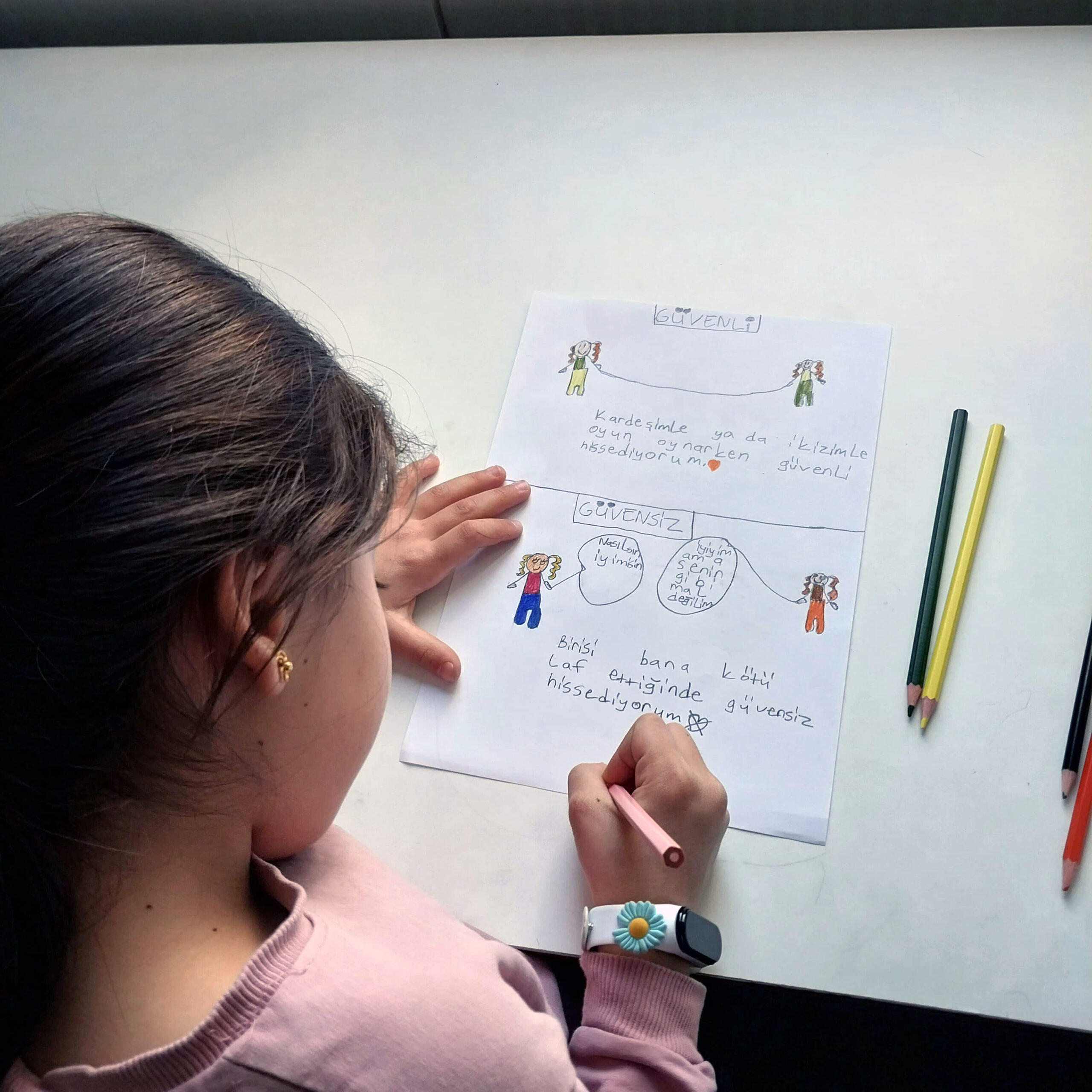 Saha çalışanımız Rojda uzun bir masada karşılıklı oturmuş birçok çocukla birlikte sanatsal etkinlik yapıyor